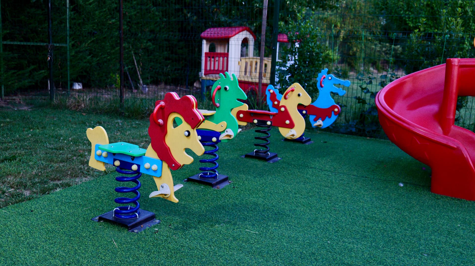 Children's playground with spring riders and a red slide on the lawn