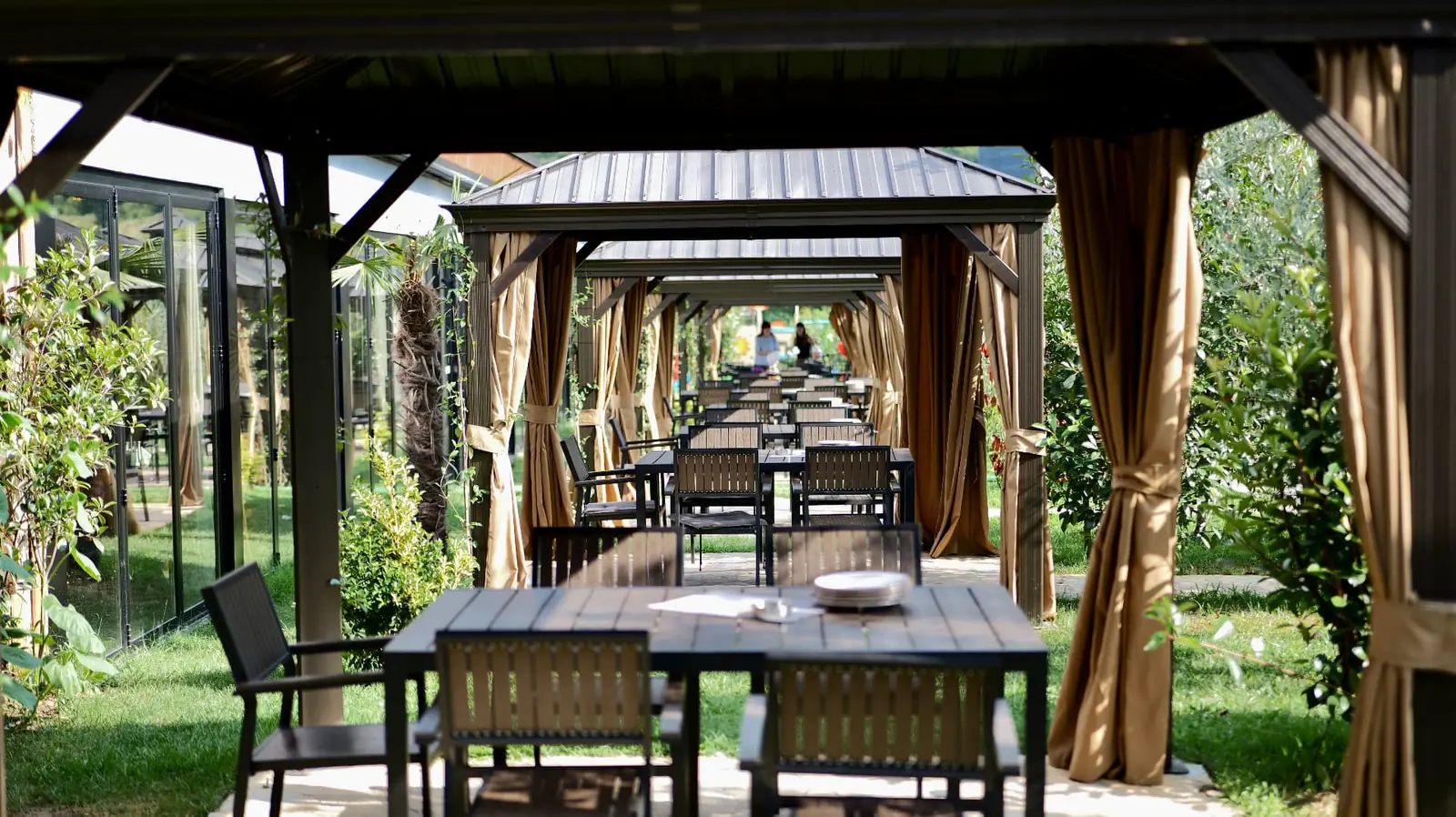Covered gazebos with curtains and set tables in the green garden of OKO Farm