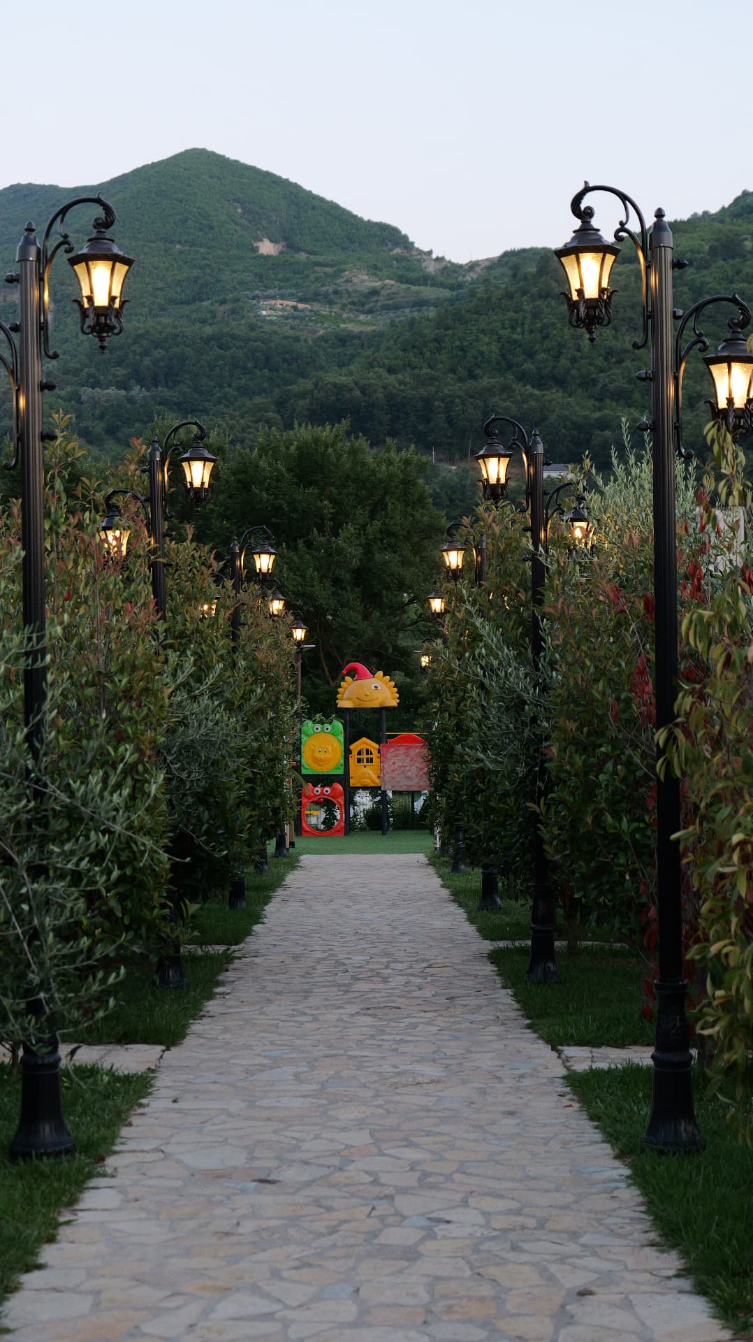 Stone path lined with lamp posts leading to the playground at dusk
