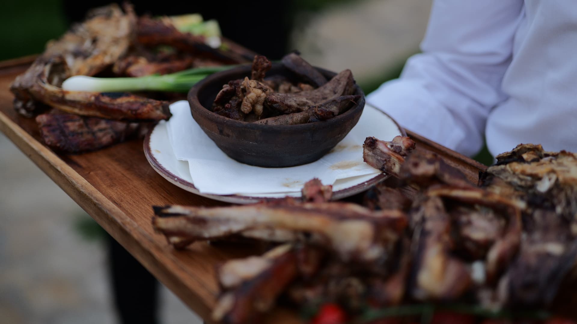 Waiter carrying a wooden board of grilled meats and spring onions at OKO Farm