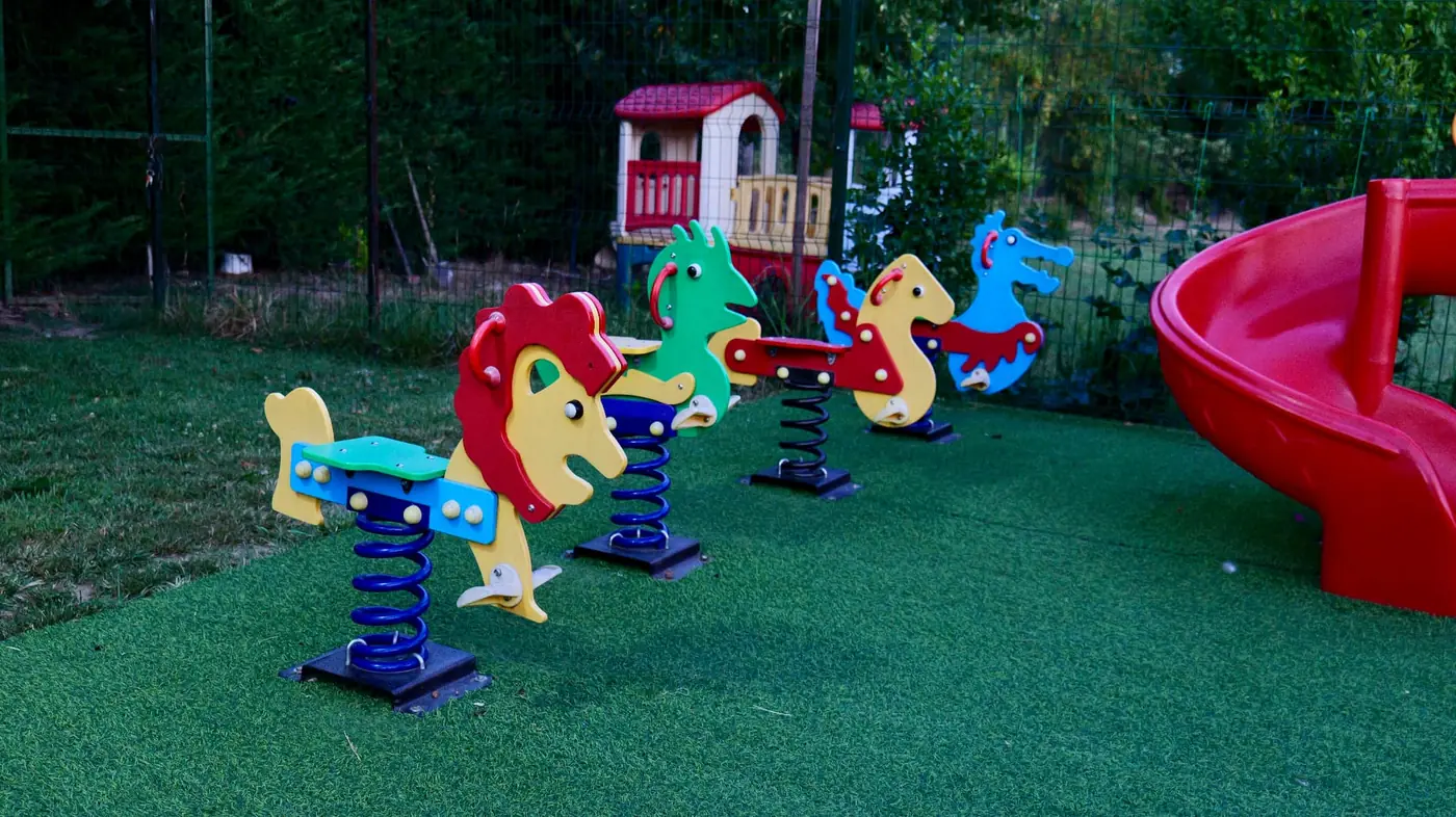 Children's playground with spring riders and a red slide on the lawn